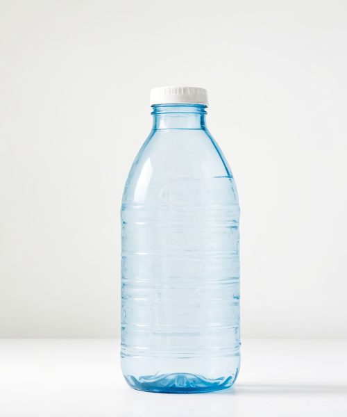 A single plastic water bottle with a white cap stands on a white surface. The bottle is clear and shows the water inside.